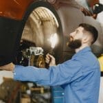 Mechanik w niebieskim kombinezonie sprawdza hamulce auta w warsztacie