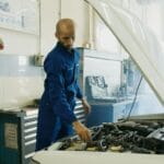 Mechanik w niebieskim kombinezonie sprawdza silnik Peugeota w warsztacie