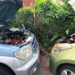 Dwa auta na parkingu połączone kablami rozruchowymi