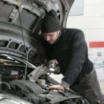 Mechanik z latarką sprawdza silnik Renault Kangoo w warsztacie