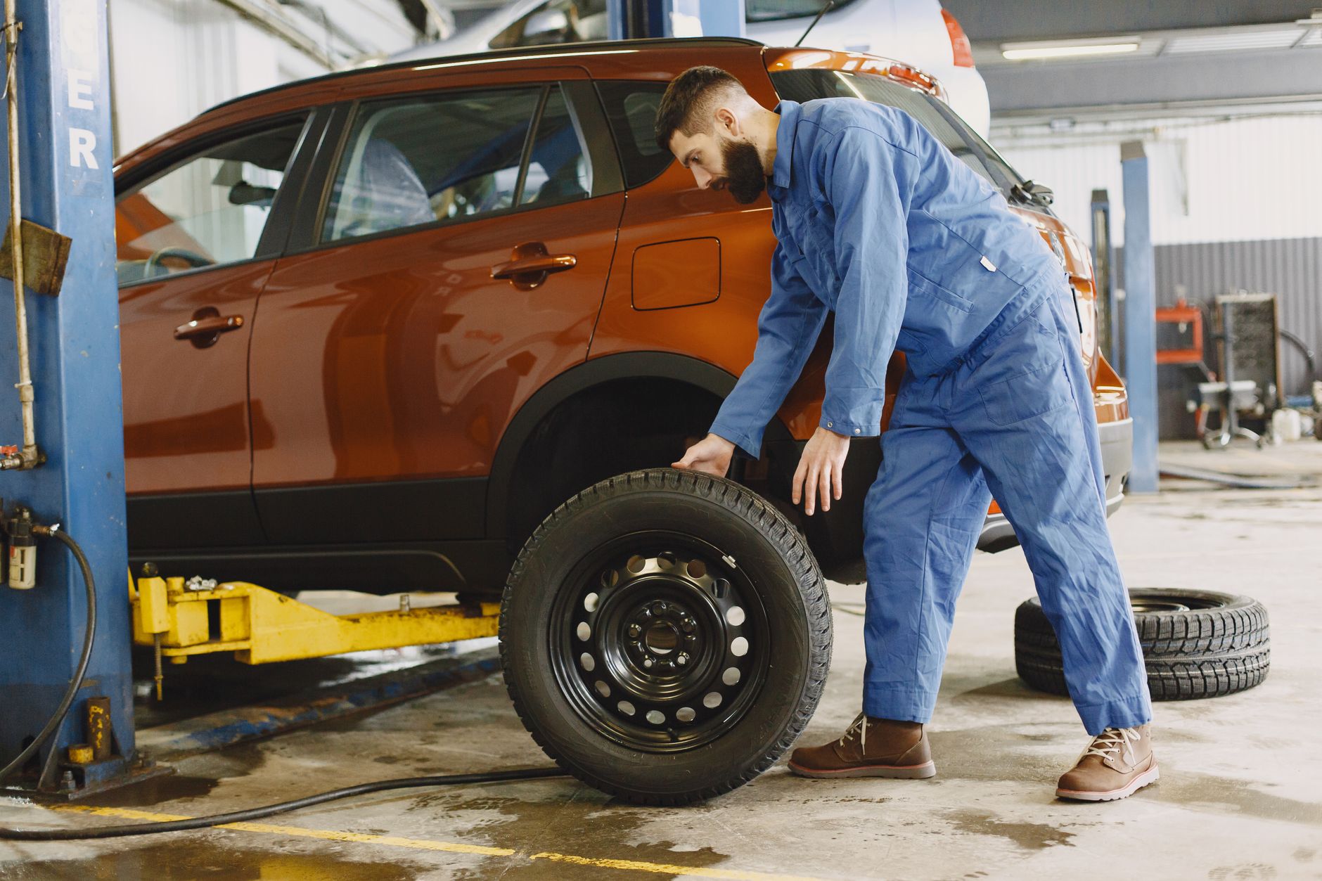 Mechanik w niebieskim kombinezonie wymienia koło w czerwonym SUV-ie